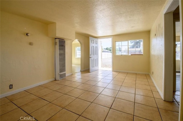spare room featuring baseboards, a textured ceiling, light tile patterned flooring, arched walkways, and a heating unit
