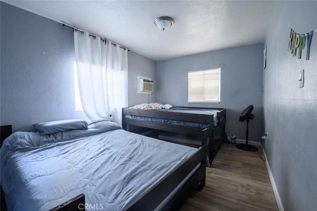 bedroom featuring a textured wall, baseboards, a wall unit AC, and wood finished floors