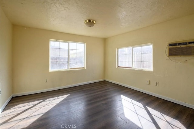 spare room with a wall mounted AC, baseboards, a textured ceiling, and wood finished floors