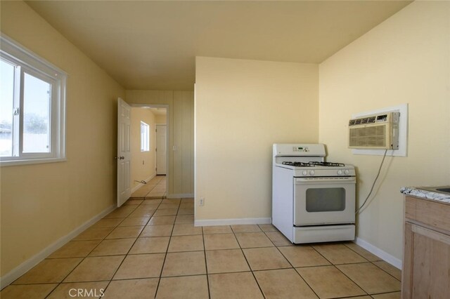 kitchen with white gas range, a wall unit AC, light tile patterned flooring, and light brown cabinets