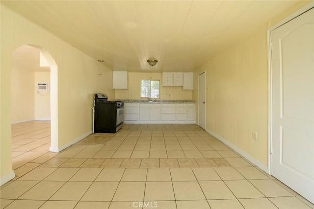 kitchen with stainless steel range with gas cooktop, arched walkways, white cabinets, light tile patterned flooring, and light countertops