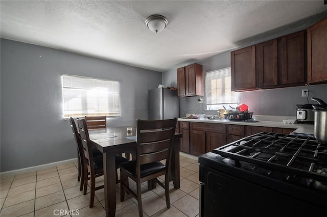 kitchen featuring stainless steel refrigerator, black range, a textured ceiling, and light tile patterned flooring