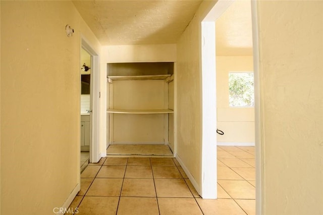 corridor with a textured ceiling, baseboards, and tile patterned flooring