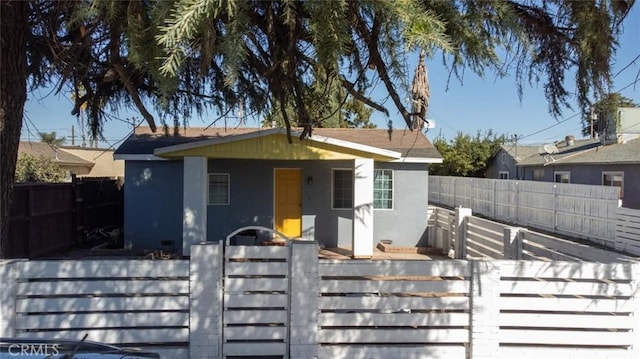 view of front facade with a fenced front yard, stucco siding, and a gate