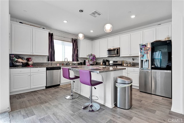 kitchen featuring light hardwood / wood-style floors, pendant lighting, a kitchen island, stainless steel appliances, and white cabinetry