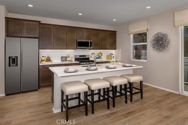 kitchen featuring a center island with sink, light hardwood / wood-style floors, dark brown cabinetry, and stainless steel appliances