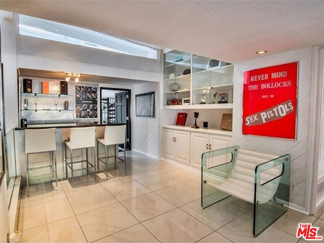 interior space with light tile patterned flooring, wooden walls, a kitchen bar, and a textured ceiling