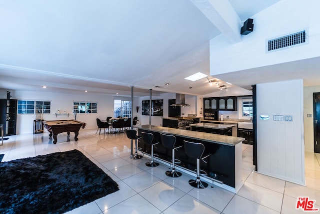 kitchen featuring pool table, light tile patterned flooring, wall chimney range hood, a breakfast bar area, and a center island