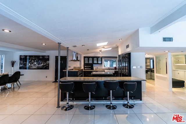 kitchen featuring a kitchen breakfast bar, light tile patterned floors, wall chimney range hood, and lofted ceiling