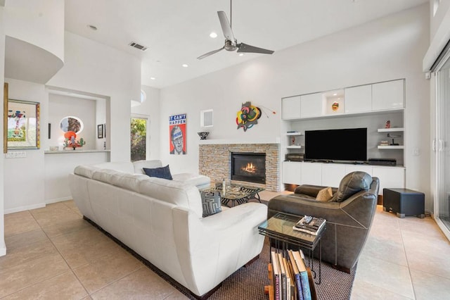 tiled living room featuring ceiling fan, a stone fireplace, and a high ceiling