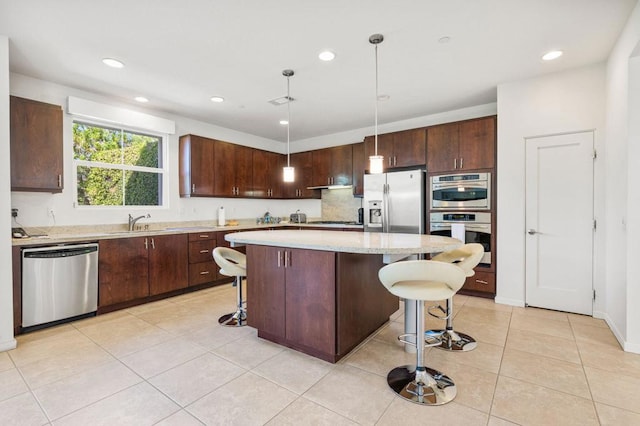 kitchen with appliances with stainless steel finishes, a kitchen breakfast bar, sink, decorative light fixtures, and a center island