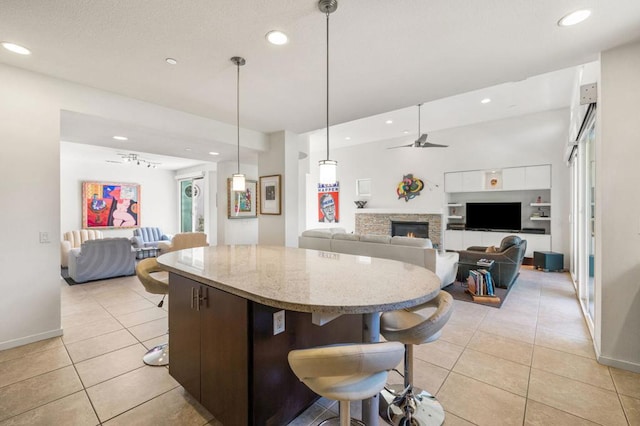 kitchen featuring a stone fireplace, ceiling fan, dark brown cabinetry, decorative light fixtures, and white cabinetry