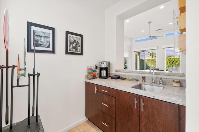 kitchen featuring sink, ceiling fan, light tile patterned floors, light stone counters, and dark brown cabinetry