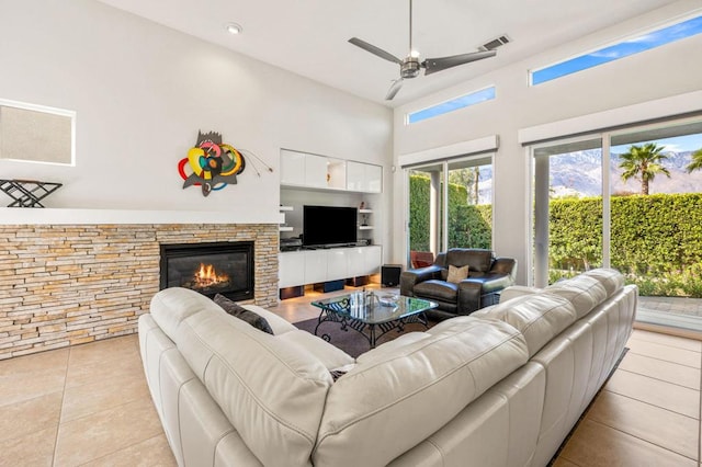 living room with a stone fireplace, ceiling fan, light tile patterned floors, and a high ceiling