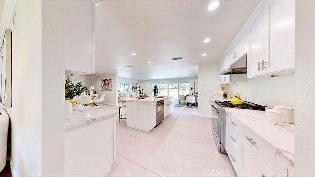 kitchen with a kitchen bar, stainless steel appliances, white cabinets, light stone countertops, and a kitchen island with sink