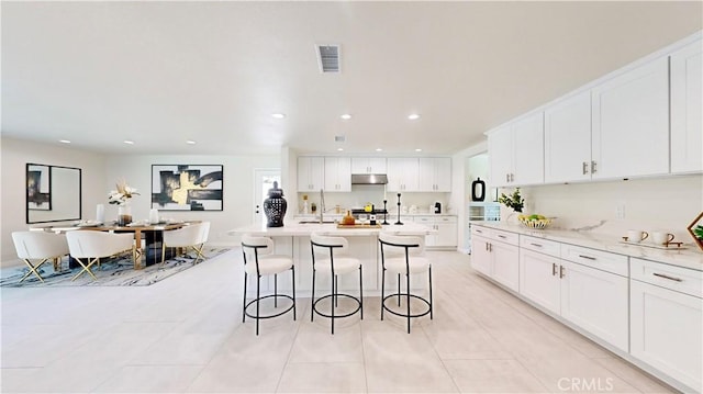 kitchen with stove, an island with sink, light stone counters, white cabinets, and a breakfast bar