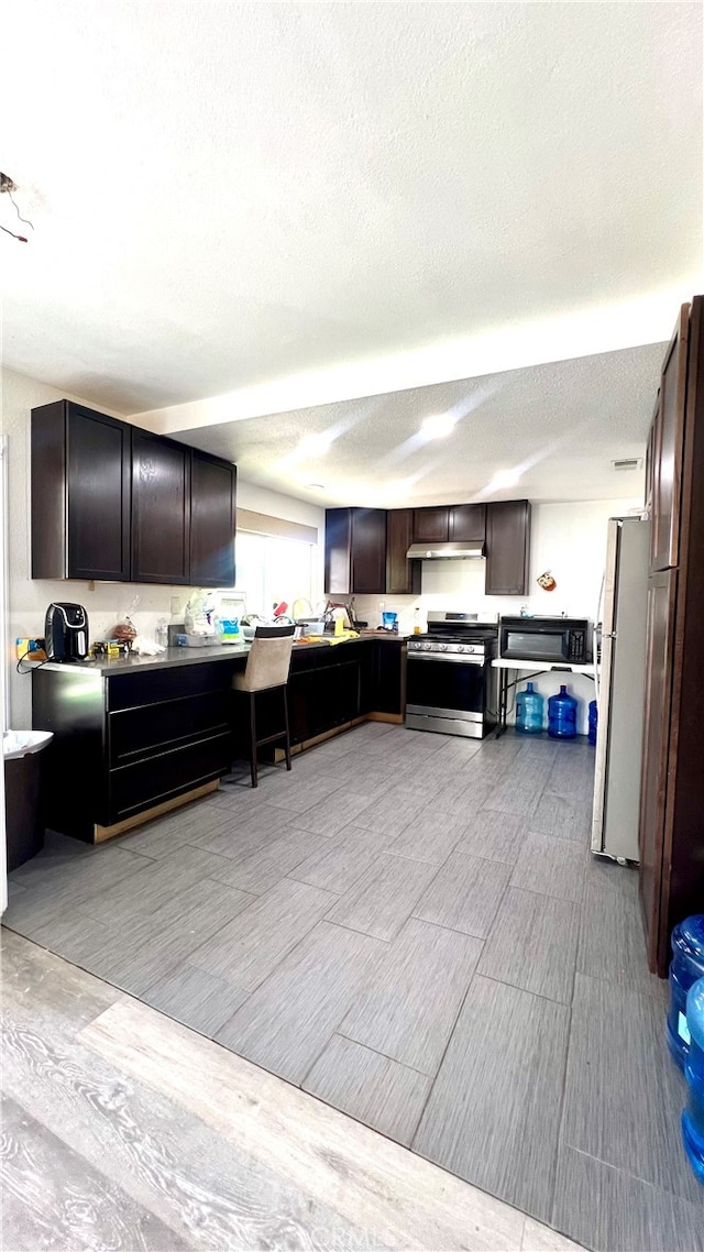 kitchen with fridge, dark brown cabinets, a textured ceiling, stainless steel range, and white refrigerator