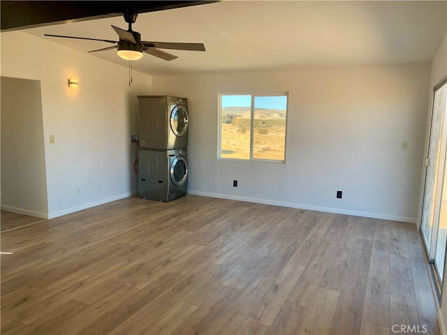 empty room featuring ceiling fan, vaulted ceiling, light wood-type flooring, and stacked washer and dryer