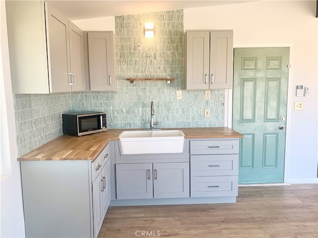 kitchen with sink, gray cabinetry, butcher block countertops, light hardwood / wood-style flooring, and vaulted ceiling