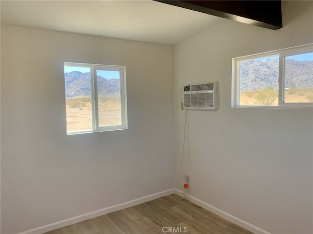 unfurnished room featuring a wall mounted AC, light wood-type flooring, a healthy amount of sunlight, and baseboards