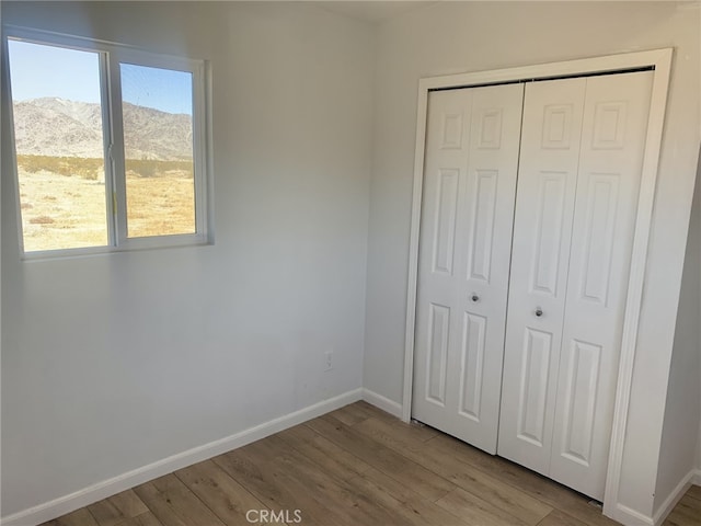unfurnished bedroom featuring a mountain view, a closet, baseboards, and wood finished floors