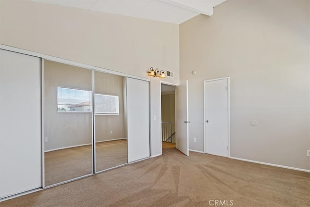 unfurnished bedroom with beamed ceiling, carpet flooring, radiator, a closet, and high vaulted ceiling