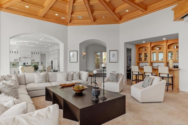 carpeted living room with a towering ceiling, beam ceiling, and wooden ceiling