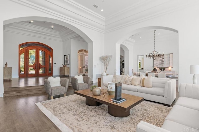 living room with french doors, crown molding, an inviting chandelier, a towering ceiling, and dark hardwood / wood-style flooring