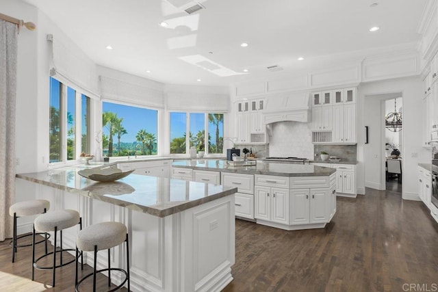 kitchen with plenty of natural light, an island with sink, white cabinets, and dark hardwood / wood-style flooring