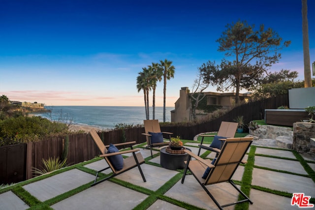 patio terrace at dusk with a water view and a fire pit