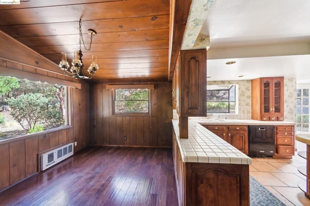 kitchen with plenty of natural light, dark wood-type flooring, wood walls, and black dishwasher