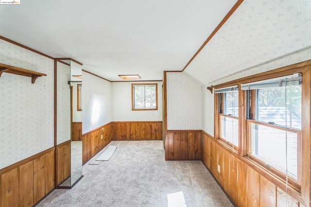 carpeted spare room with wood walls, ornamental molding, and a healthy amount of sunlight