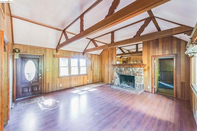 unfurnished living room featuring lofted ceiling with beams, wood walls, a stone fireplace, and wood-type flooring