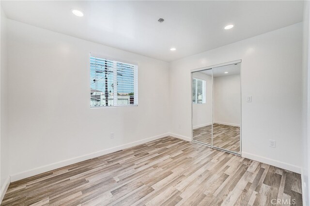 unfurnished bedroom with light wood-type flooring, a closet, and multiple windows