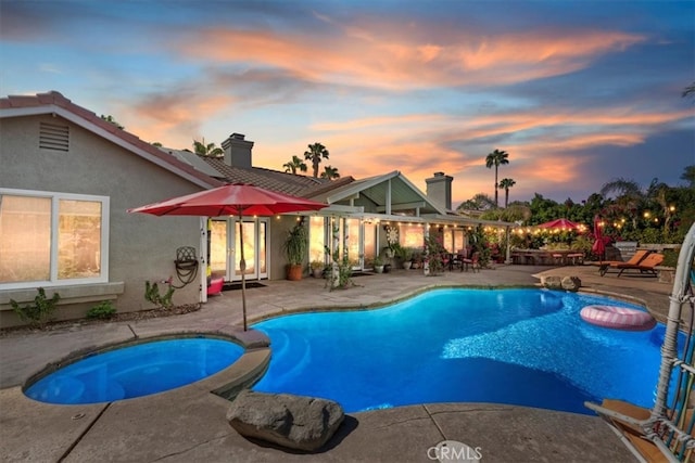 pool at dusk featuring an in ground hot tub and a patio area