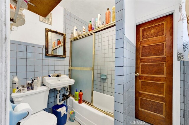 full bathroom with sink, toilet, tile walls, and bath / shower combo with glass door