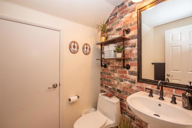 bathroom with brick wall, sink, and toilet