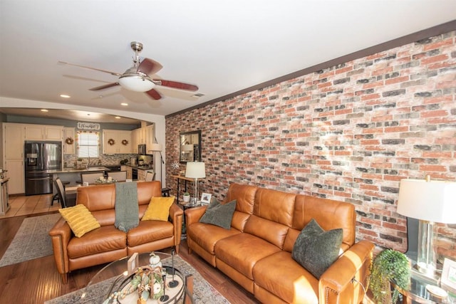 living room featuring brick wall, light wood-type flooring, and ceiling fan