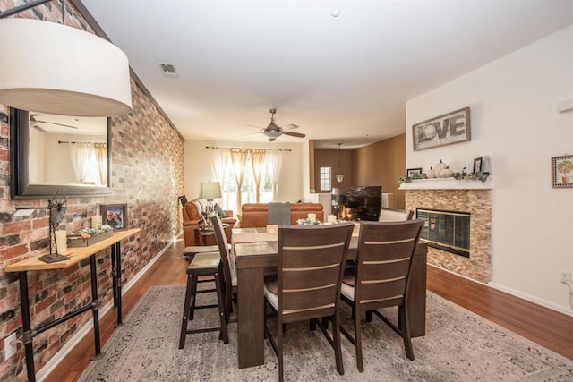 dining space featuring wood-type flooring, brick wall, and ceiling fan