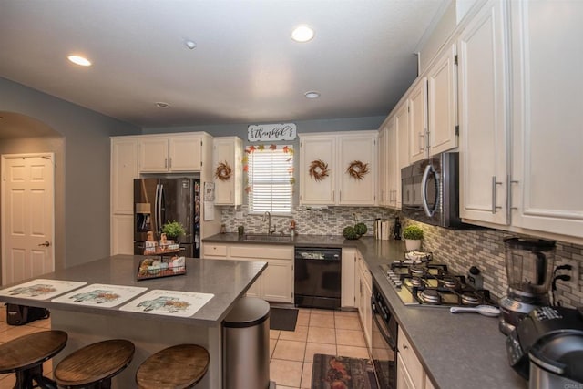 kitchen with black appliances, a center island, sink, white cabinetry, and light tile patterned floors