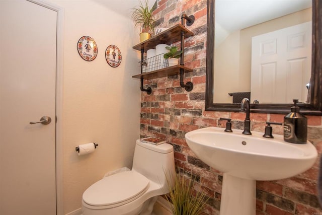 bathroom with brick wall, sink, and toilet