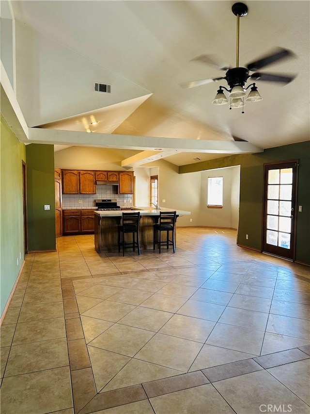 kitchen with backsplash, vaulted ceiling, ceiling fan, a kitchen island, and a kitchen bar