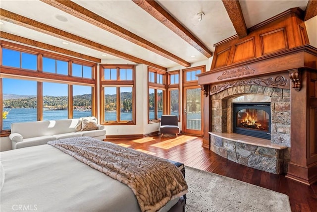 bedroom with hardwood / wood-style floors, beamed ceiling, a water view, and a fireplace