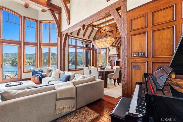 living room featuring beamed ceiling, an inviting chandelier, a high ceiling, hardwood / wood-style flooring, and a water view