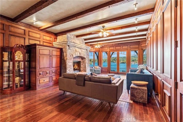 living room with wooden walls, dark hardwood / wood-style floors, a fireplace, a water view, and beamed ceiling