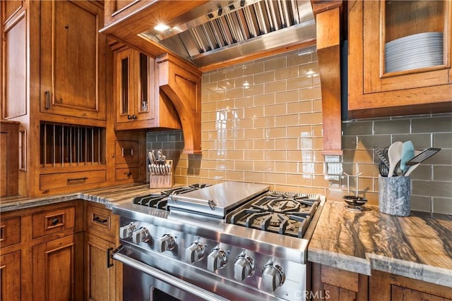 kitchen with high end stainless steel range oven, stone countertops, decorative backsplash, and wall chimney exhaust hood