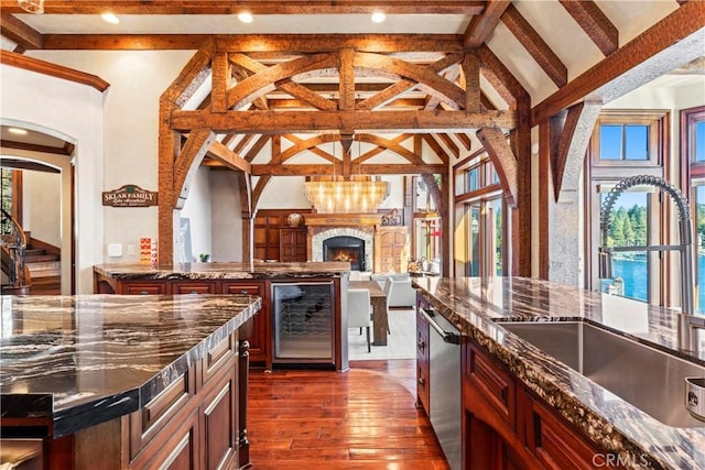 kitchen with a water view, dark stone countertops, beverage cooler, beam ceiling, and sink