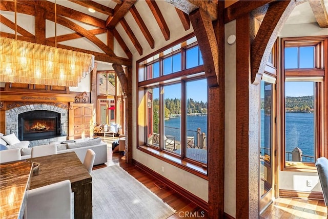 sunroom featuring a water view, vaulted ceiling with beams, an inviting chandelier, and a stone fireplace