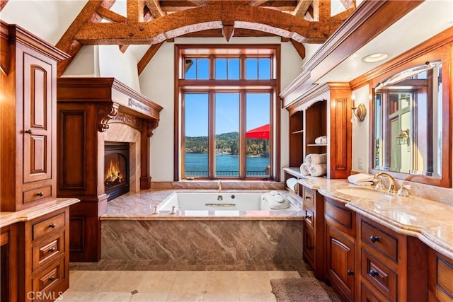 bathroom with a high end fireplace, a towering ceiling, vanity, a water view, and a relaxing tiled tub