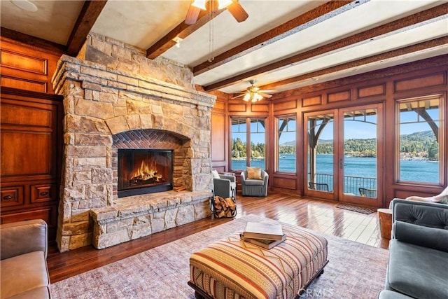 living room featuring hardwood / wood-style flooring, a stone fireplace, a water view, french doors, and beam ceiling